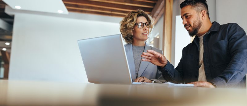 Two people sat in an office discussing something on a laptop