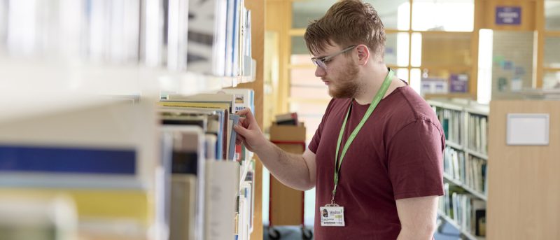 Moulton College student picking at bookshelf at the learning hub / library