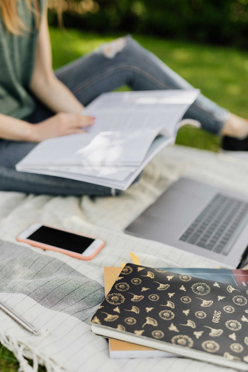 Students studying outside with a pile of books and laptop. Taken  by Karolina Grabowska