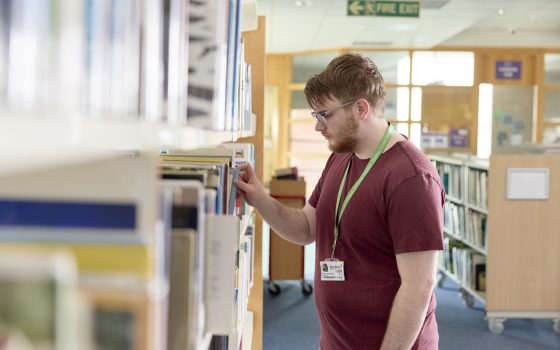 Moulton College student picking at bookshelf at the learning hub / library