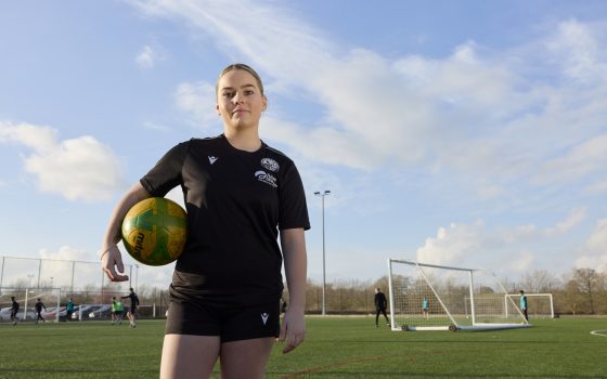 Sports student holding football on astro pitch